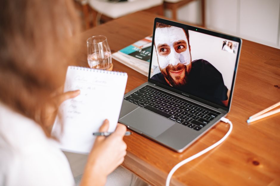 A man in a facial mask on a video call with a woman taking notes by a laptop. - Photo by ROMAN ODINTSOV on Pexels