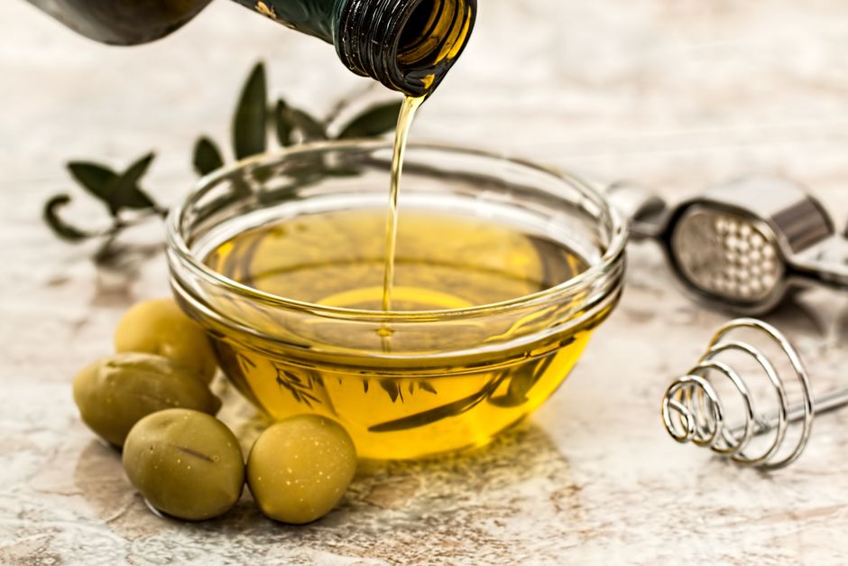 Close-up of olive oil being poured into a glass bowl surrounded by fresh olives and kitchen tools. - Photo by Pixabay on Pexels